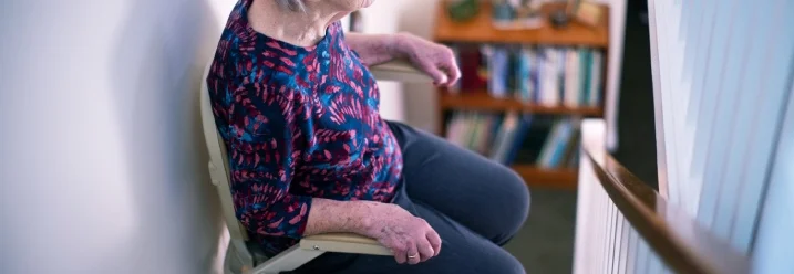 Ältere Person sitzt in einem Treppenlift auf einer Treppe.